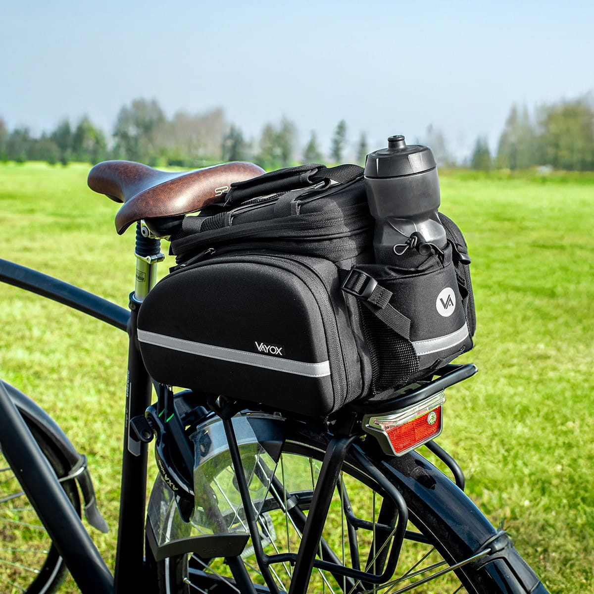 Czarna torba rowerowa na rowerze, z uchwytem na butelkę, na zielonym polu, brązowe siodełko.