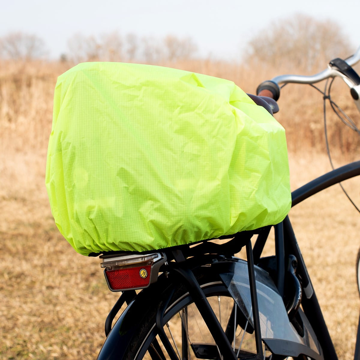 Rower z żółtą osłoną na tylnym koszu, w otoczeniu pola.