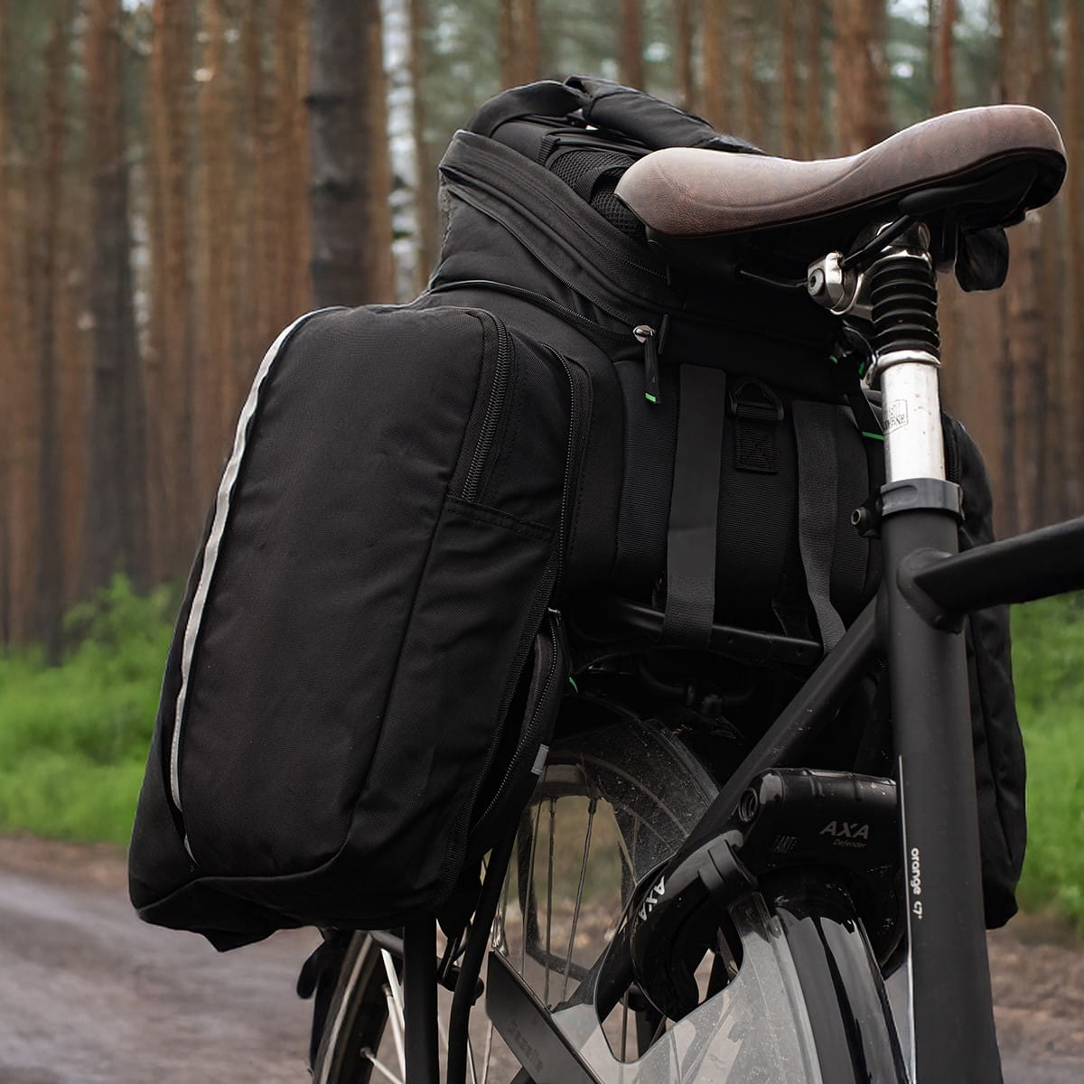 Czarny rower z tylną torbą. Zdjęcie zrobione w lesie z rozmytym tłem.