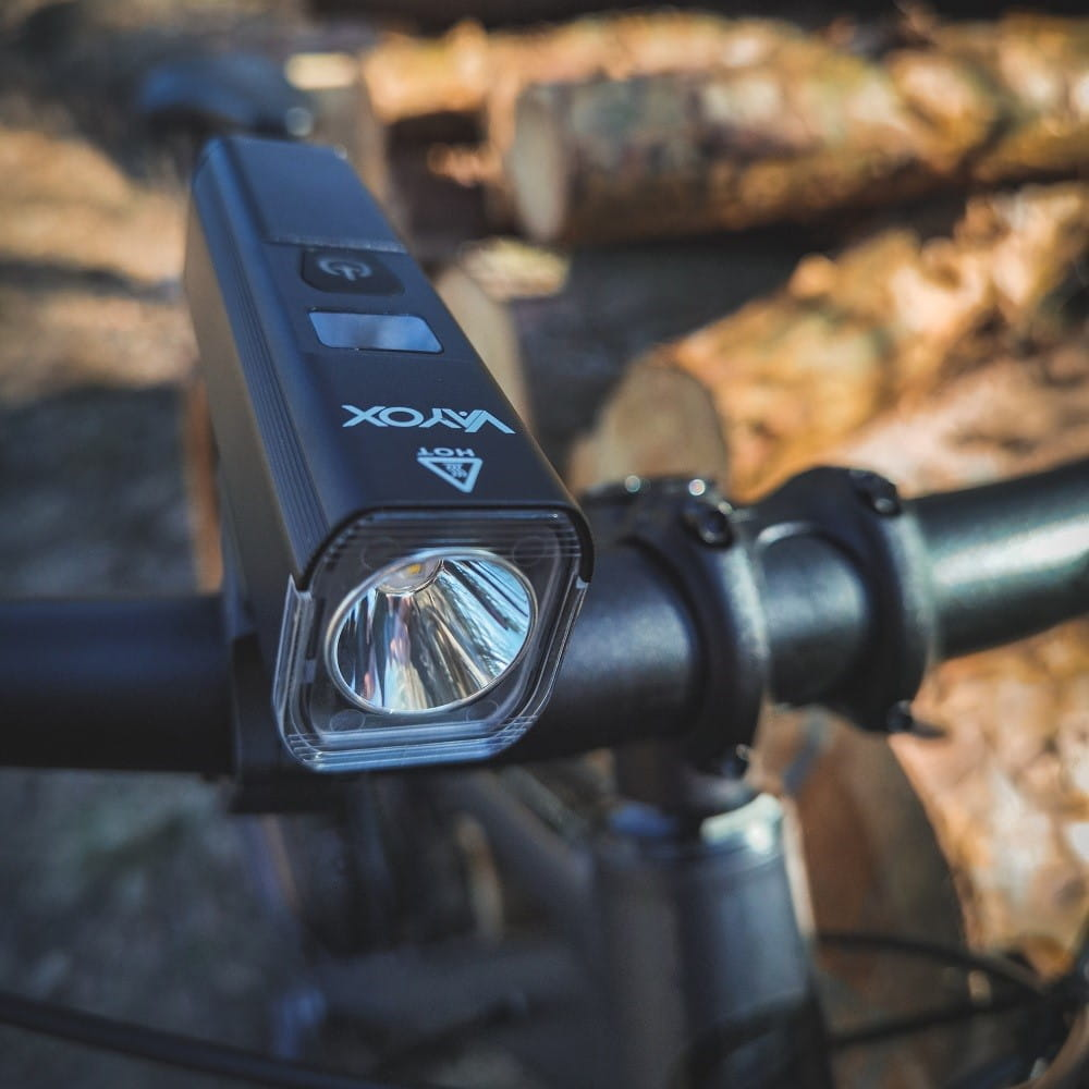 Czarne światło rowerowe przymocowane do kierownicy, skupione światłem. Kłody w tle.