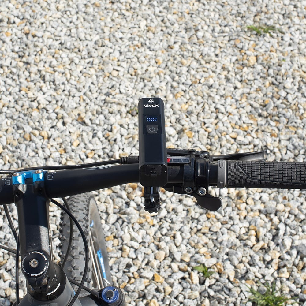 Czarna lampka rowerowa zamontowana na kierownicy. Tło żwirowe.