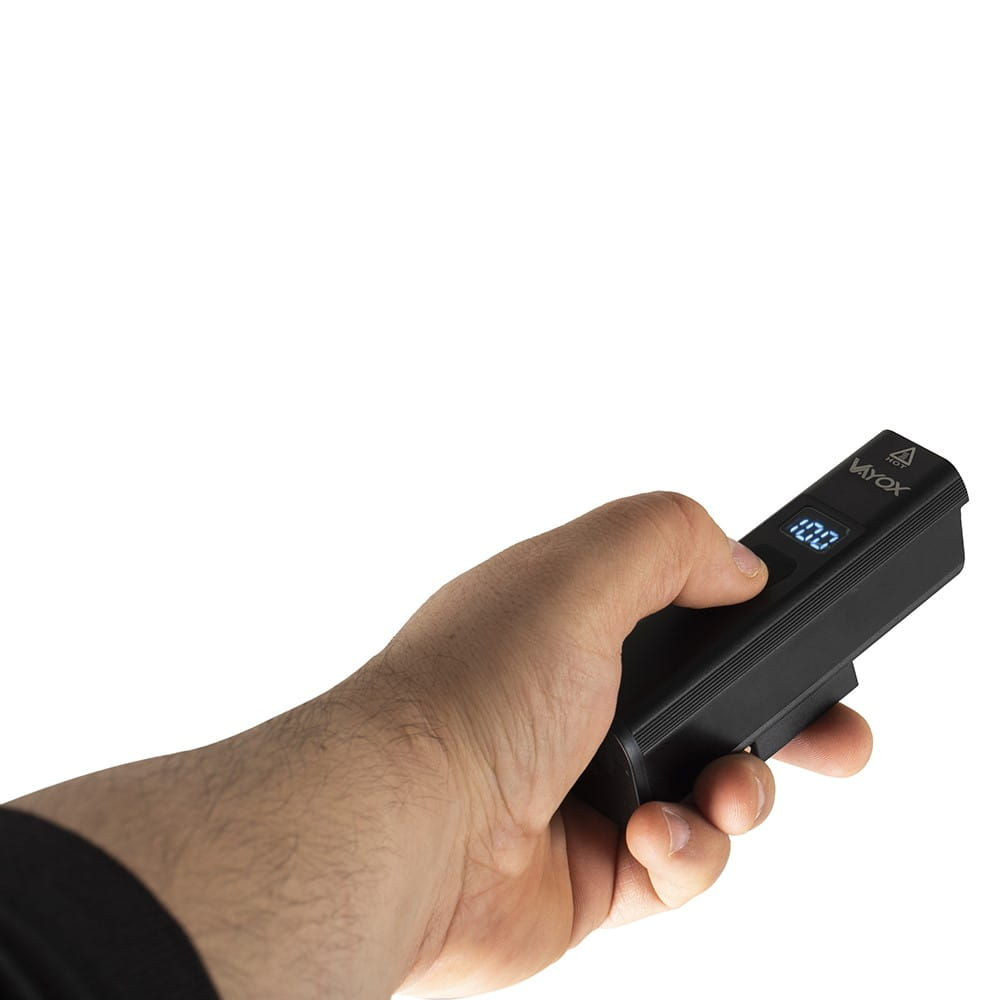 Ręka trzymająca czarne urządzenie z wyświetlaczem cyfrowym na białym tle.