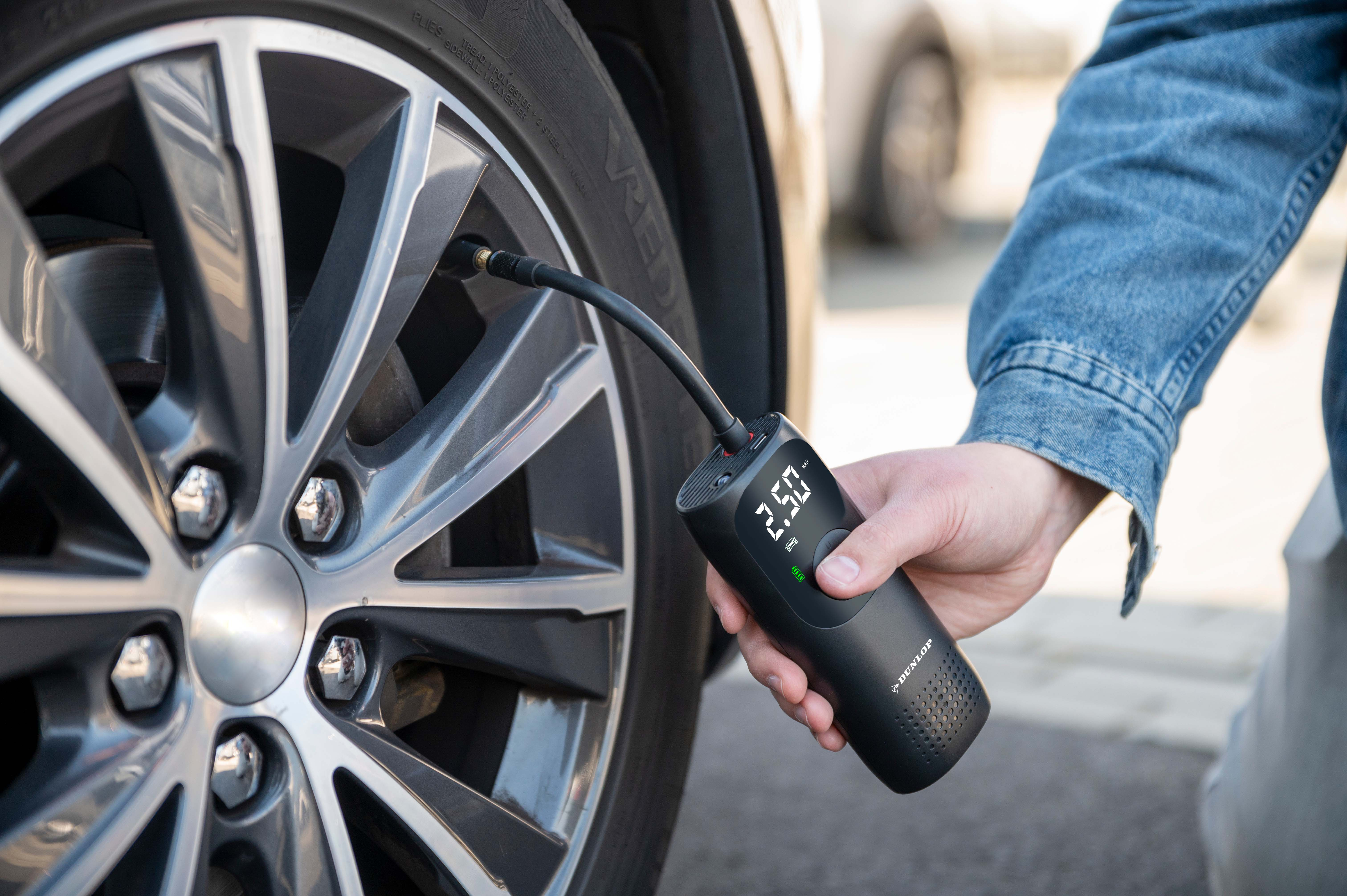 Person using a Dunlop air compressor to inflate a car tire. The display shows 2.50 bar.