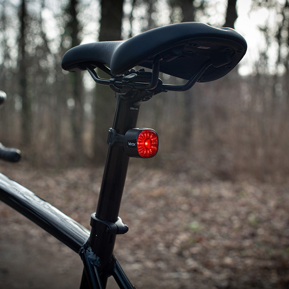 Czerwone światło rowerowe Vayox przymocowane do czarnej sztycy. Drzewa w tle.