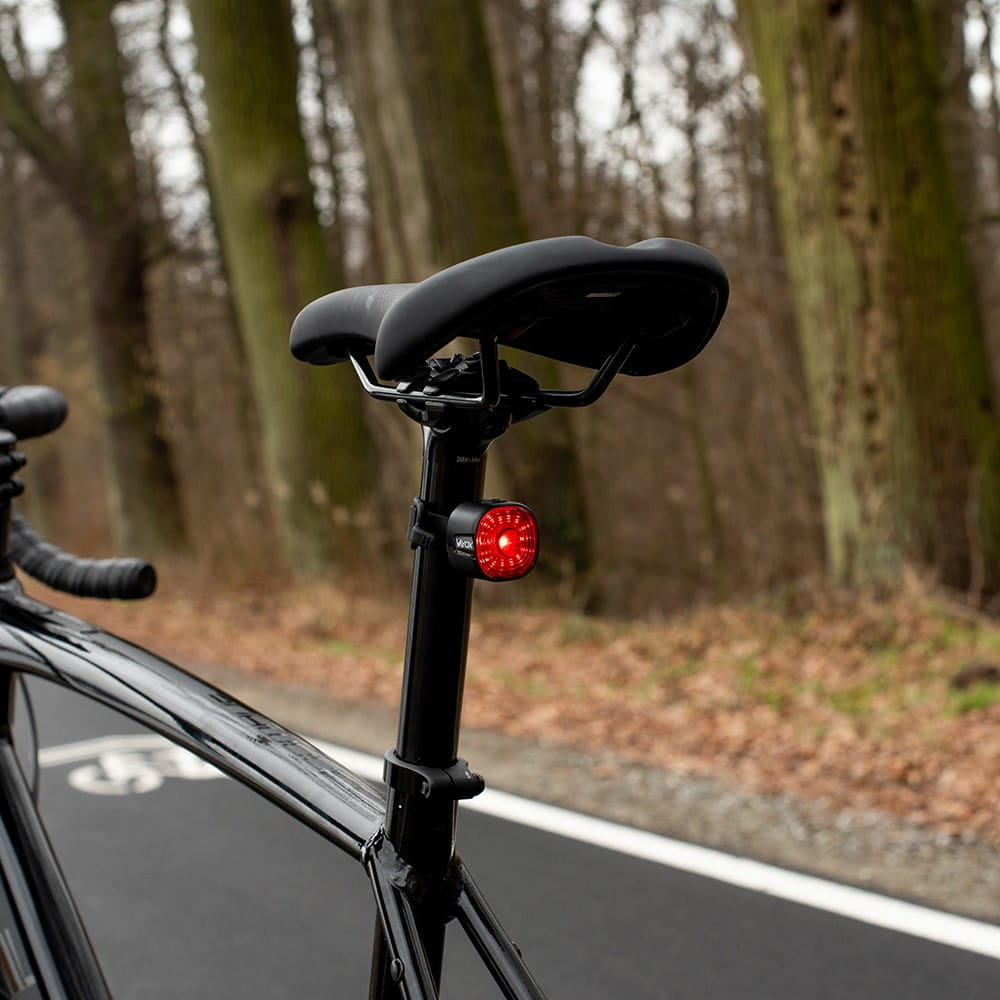 Rower z czerwonym tylnym światłem na sztycy, na utwardzonej drodze.