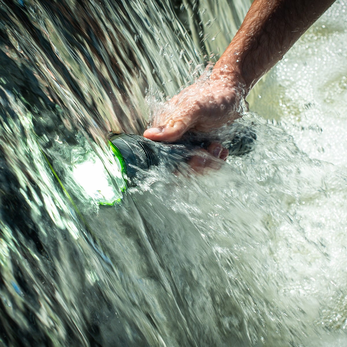 Ręka trzymająca latarkę w płynącej wodzie. Światło jest włączone.