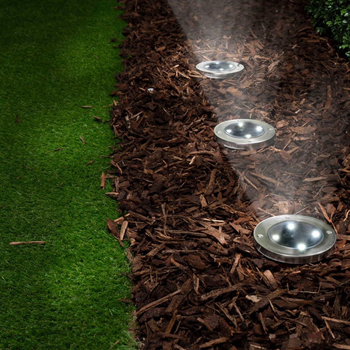 Garden path with three round lights on wood chips. Green grass on the left.