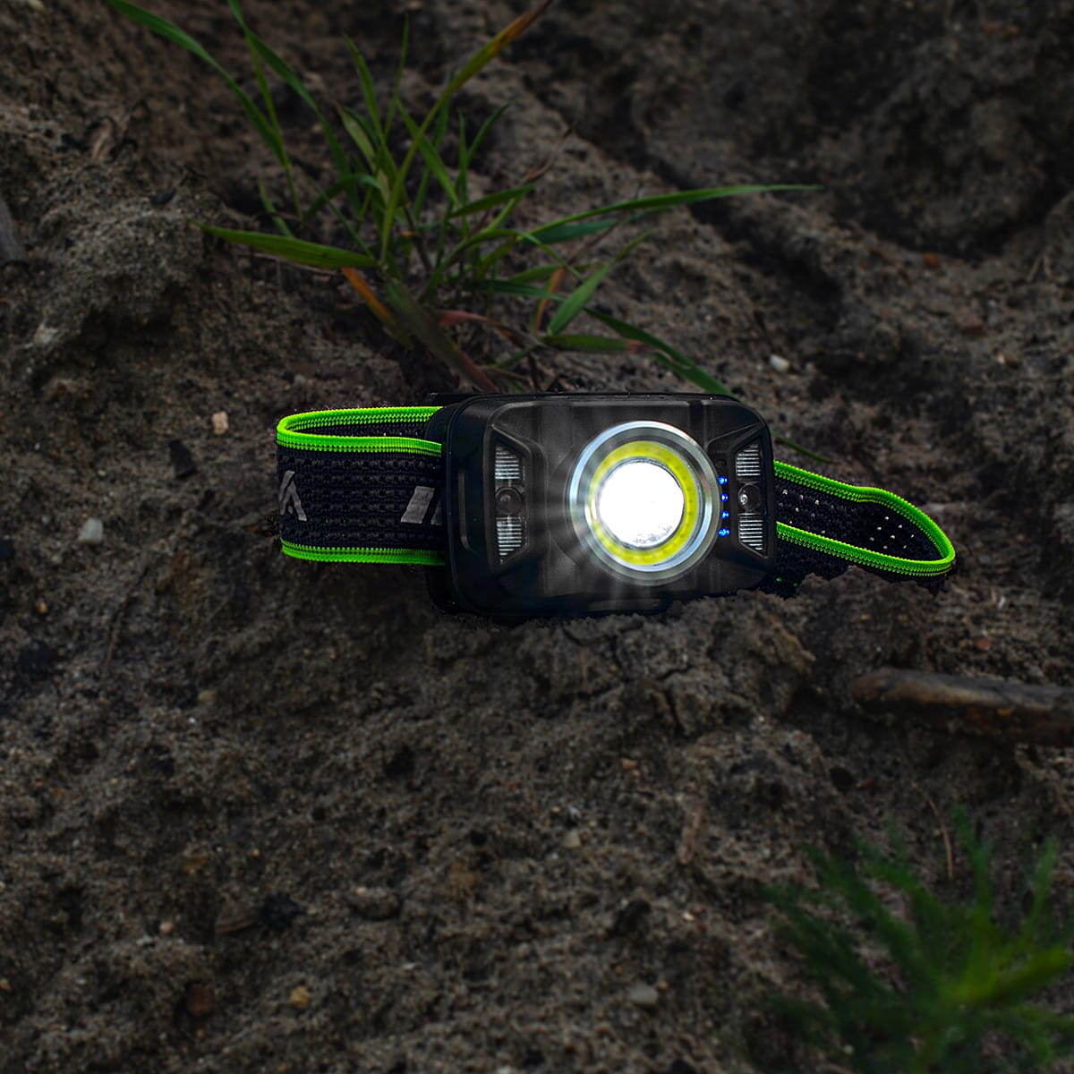 Czarna latarka czołowa na ziemi. Światło jest włączone, z zielono-czarnym paskiem.