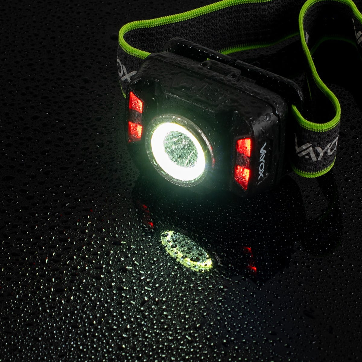 Zbliżenie na latarkę czołową. Światło jest włączone, z kroplami wody i czarnym paskiem.