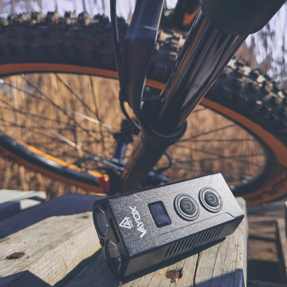 Czarna latarka zamontowana na drewnianej powierzchni, w pobliżu koła roweru. Ma ekran.