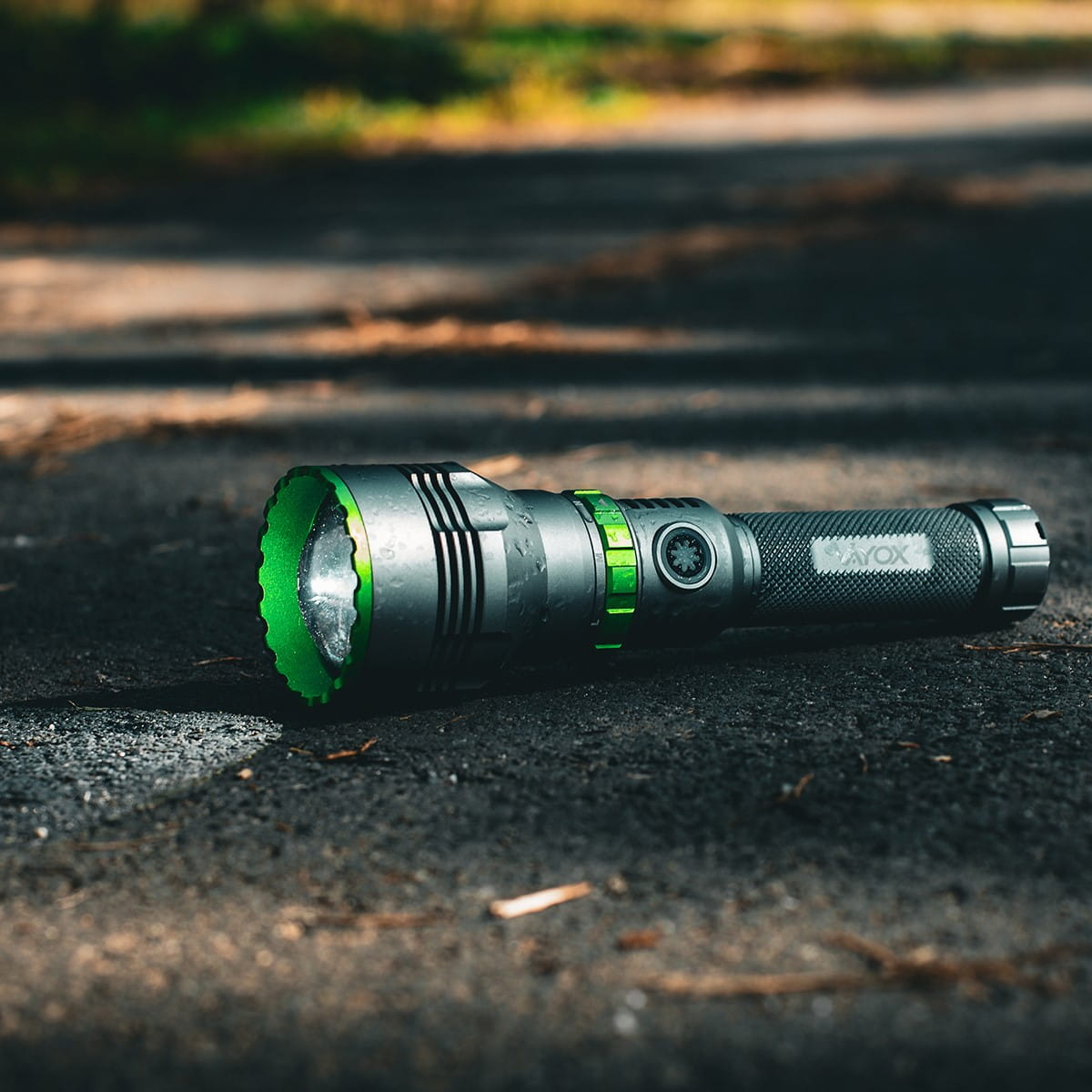 Czarna i zielona latarka na drodze. Światło jest włączone. Na pierwszym planie jest asfalt.