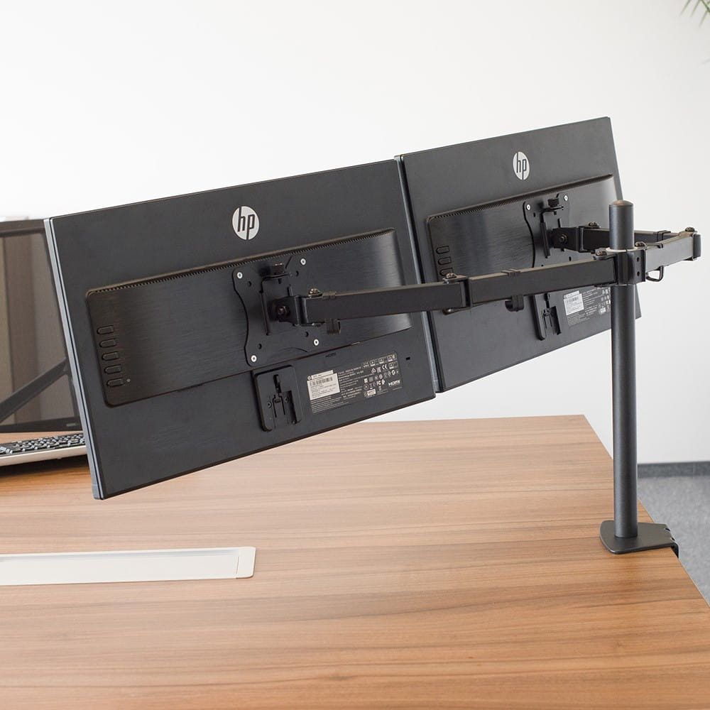 Dwa czarne monitory komputerowe są przymocowane do biurka za pomocą uchwytu. Uchwyt ma regulowane ramiona.