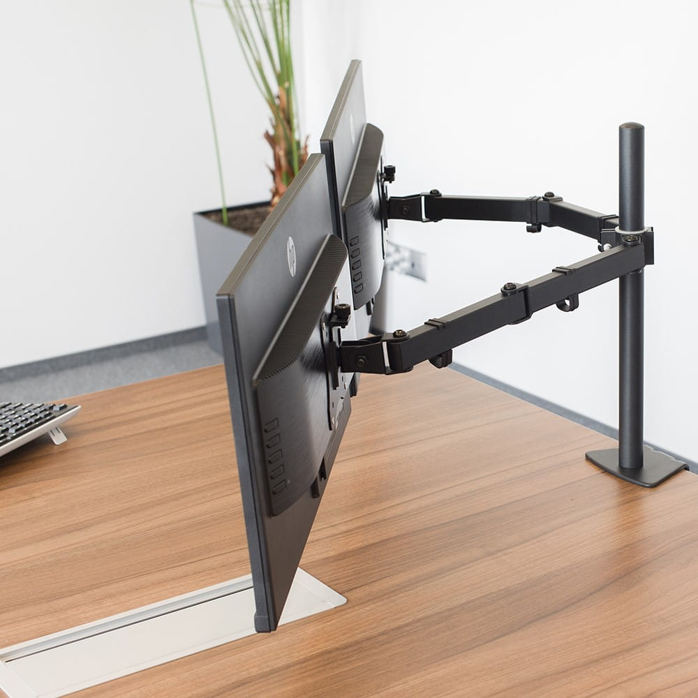 Dwa monitory komputera zamontowane na czarnym ramieniu biurka, na brązowym biurku.