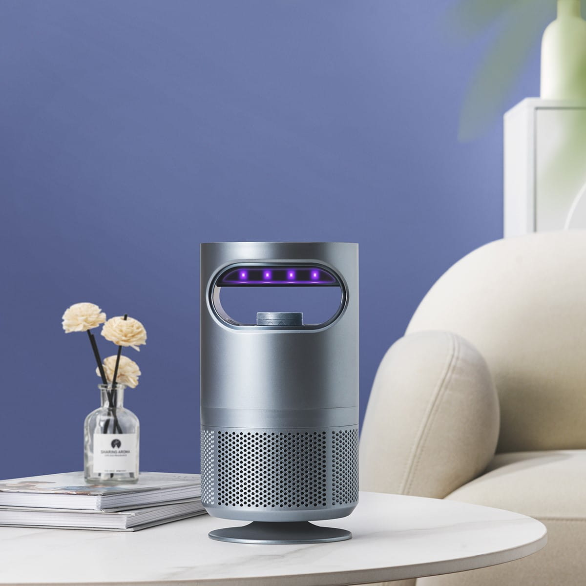 Srebrna lampa owadobójcza na stole z wazonem kwiatów na tle niebieskiej ściany i białej sofy.