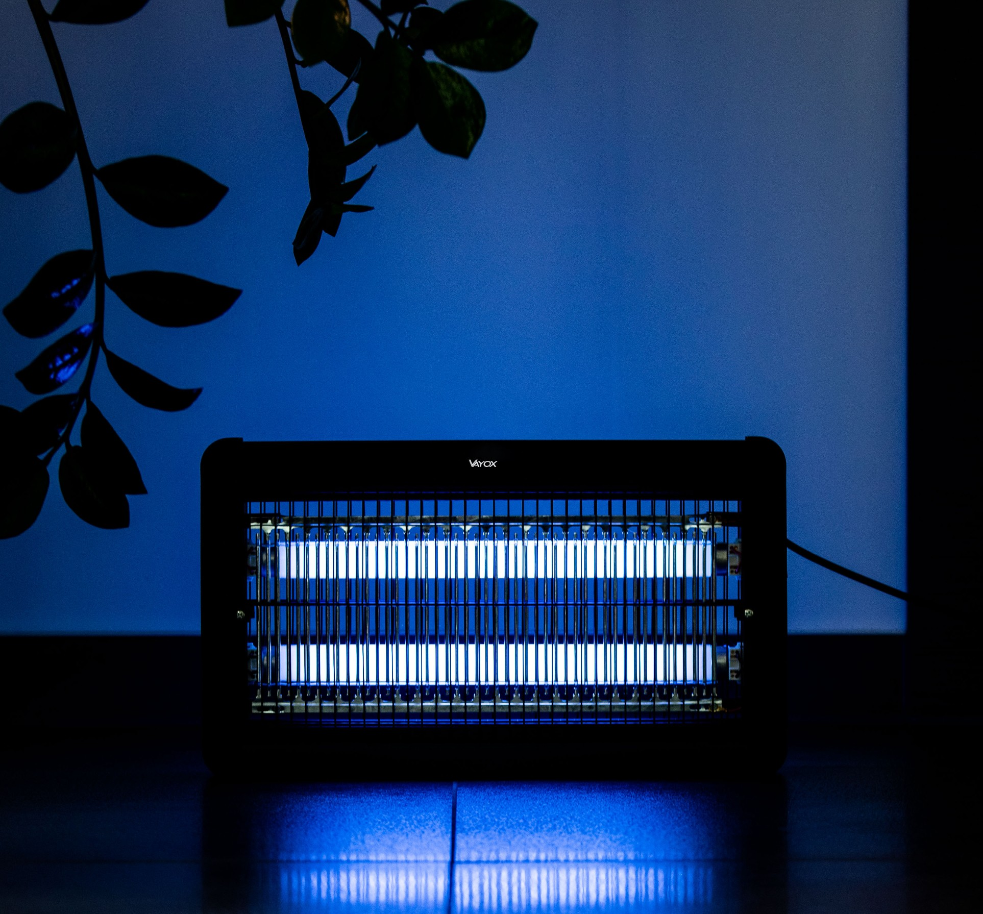 Elektryczny zabójca owadów z niebieskimi światłami UV, na drewnianym stole. Roślina w tle.