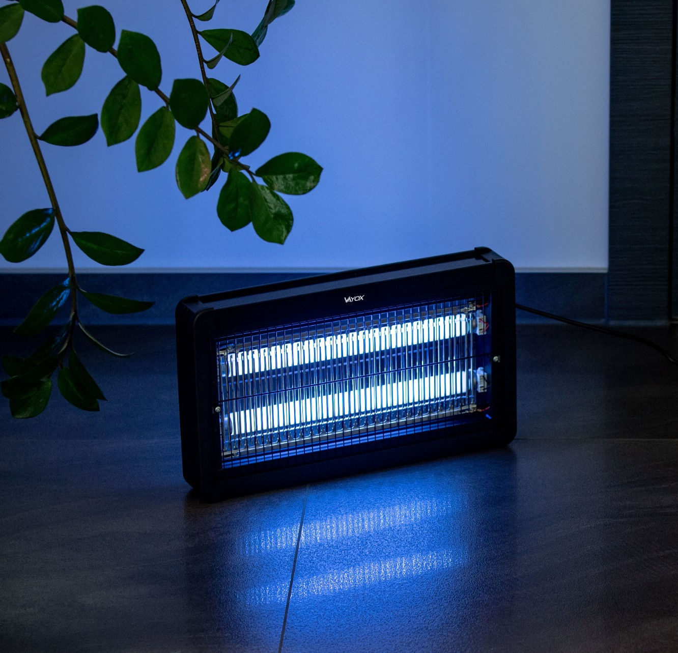 Zabijacz owadów z niebieskim światłem UV na podłodze, z rośliną w tle.
