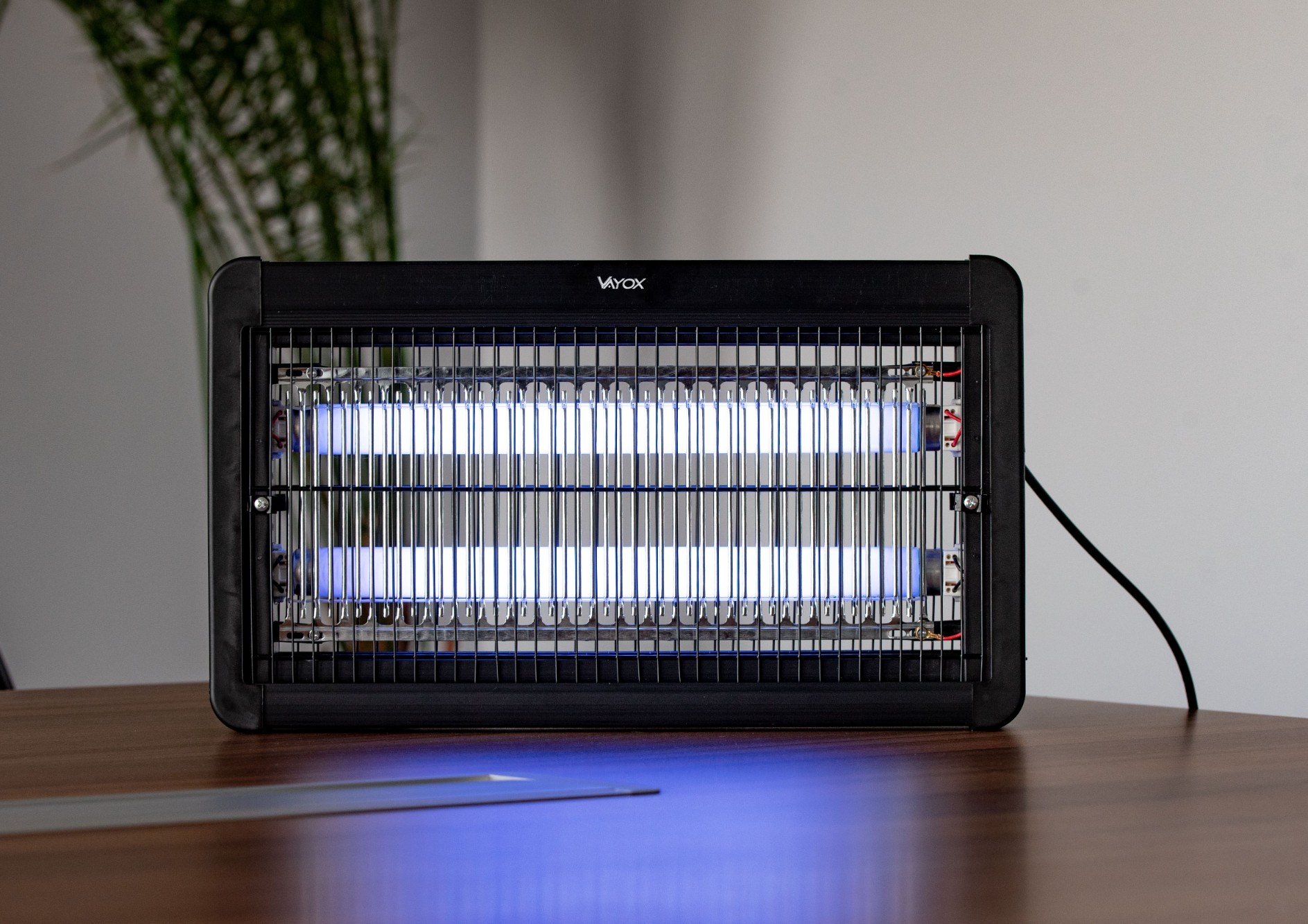 Zabijacz owadów z niebieskim światłem UV na drewnianym stole. Widoczne logo 'Vayox'.