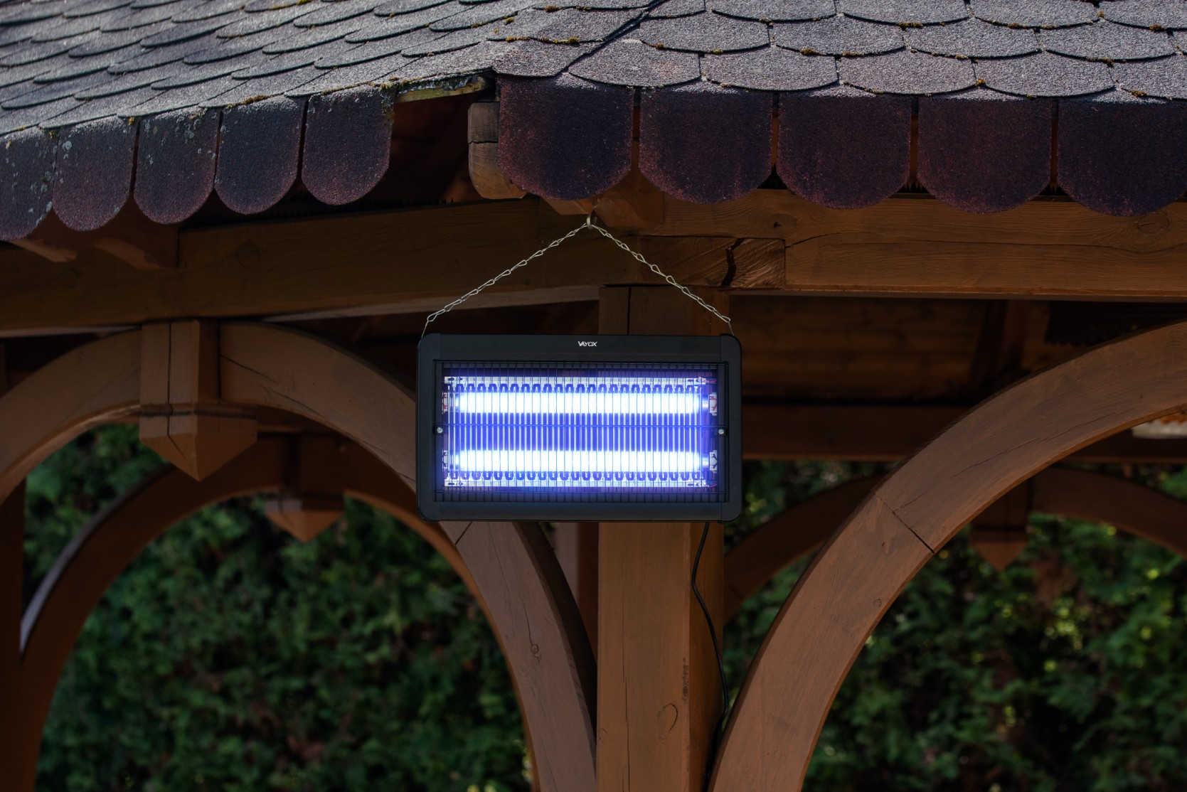 Czarny zabójca owadów wisi pod drewnianą konstrukcją, z włączonym niebieskim światłem.