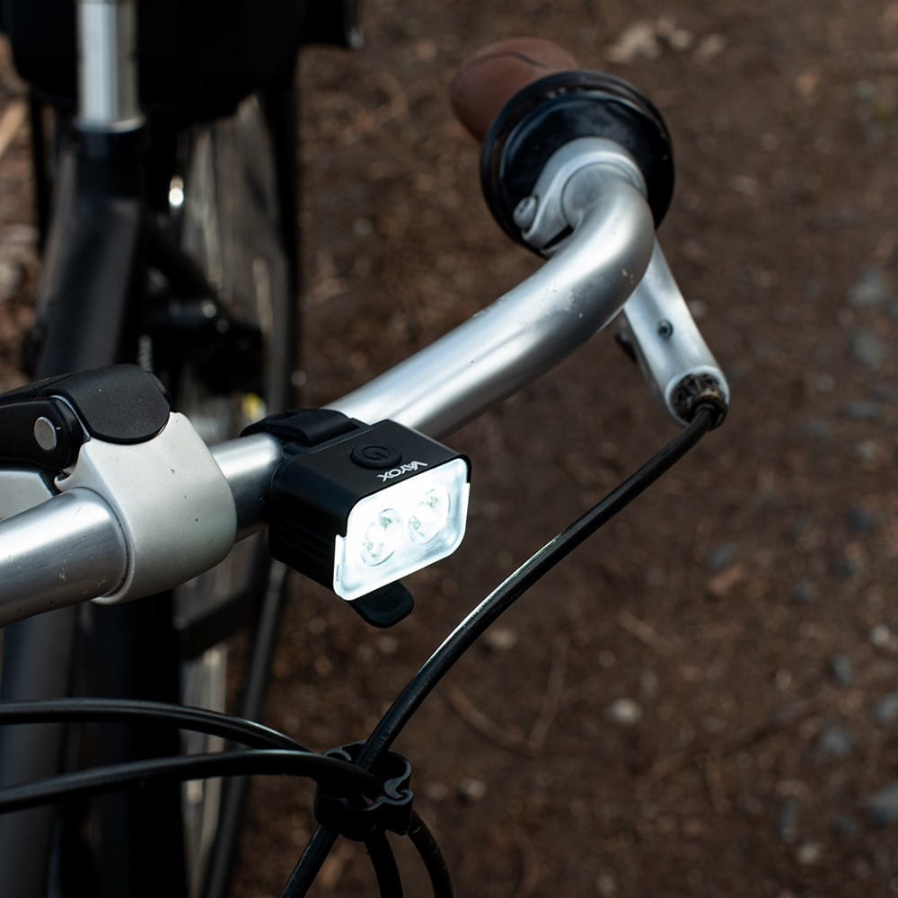 Światło rowerowe zamontowane na kierownicy. Światło jest czarne i ma dwie diody LED.