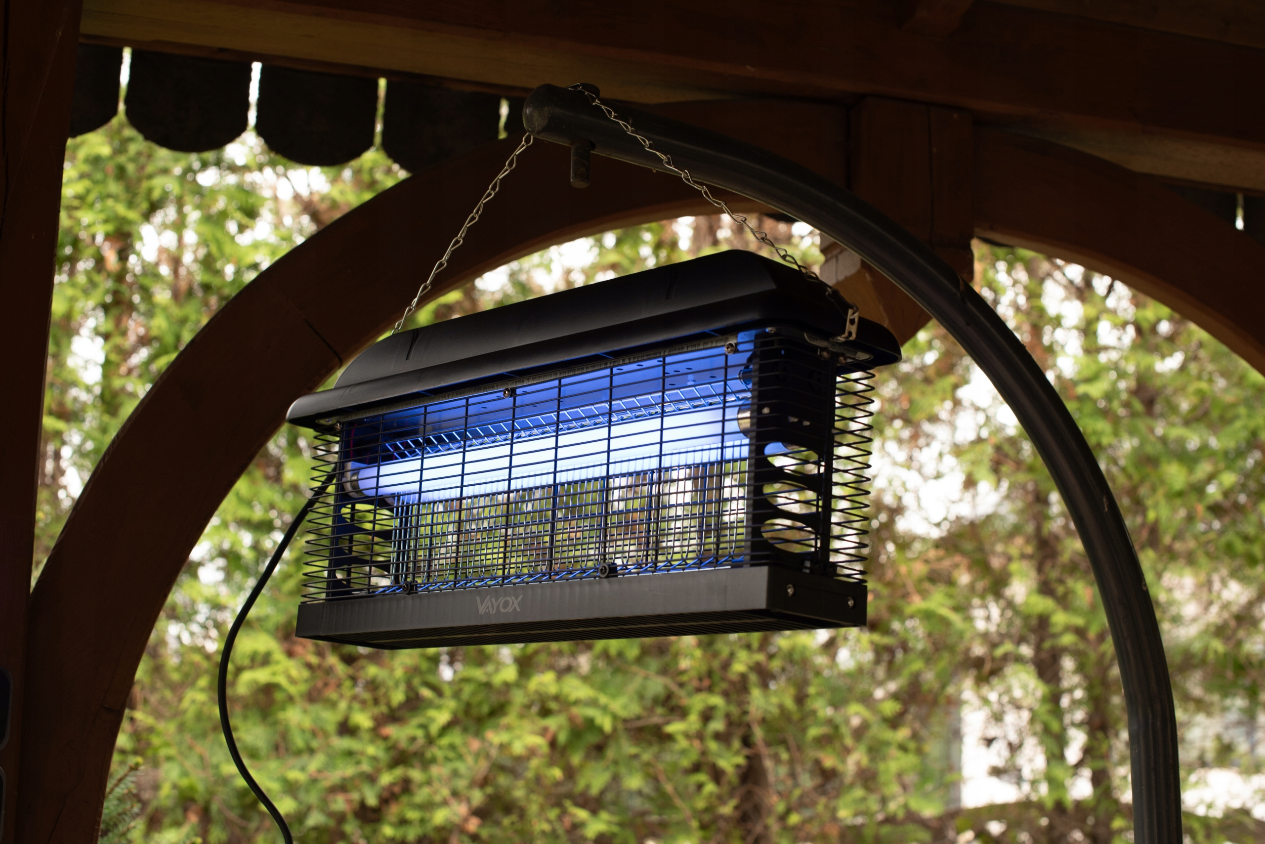 Czarny zapper na owady pod drewnianą konstrukcją z zielonym tłem.