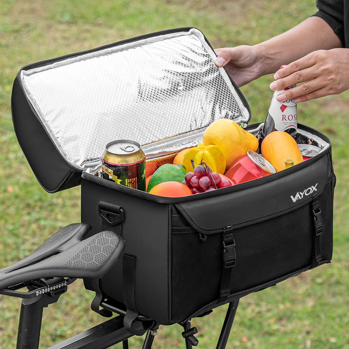 Otwarta torba rowerowa z owocami, napojami. Czarna torba na siedzeniu, ręka.