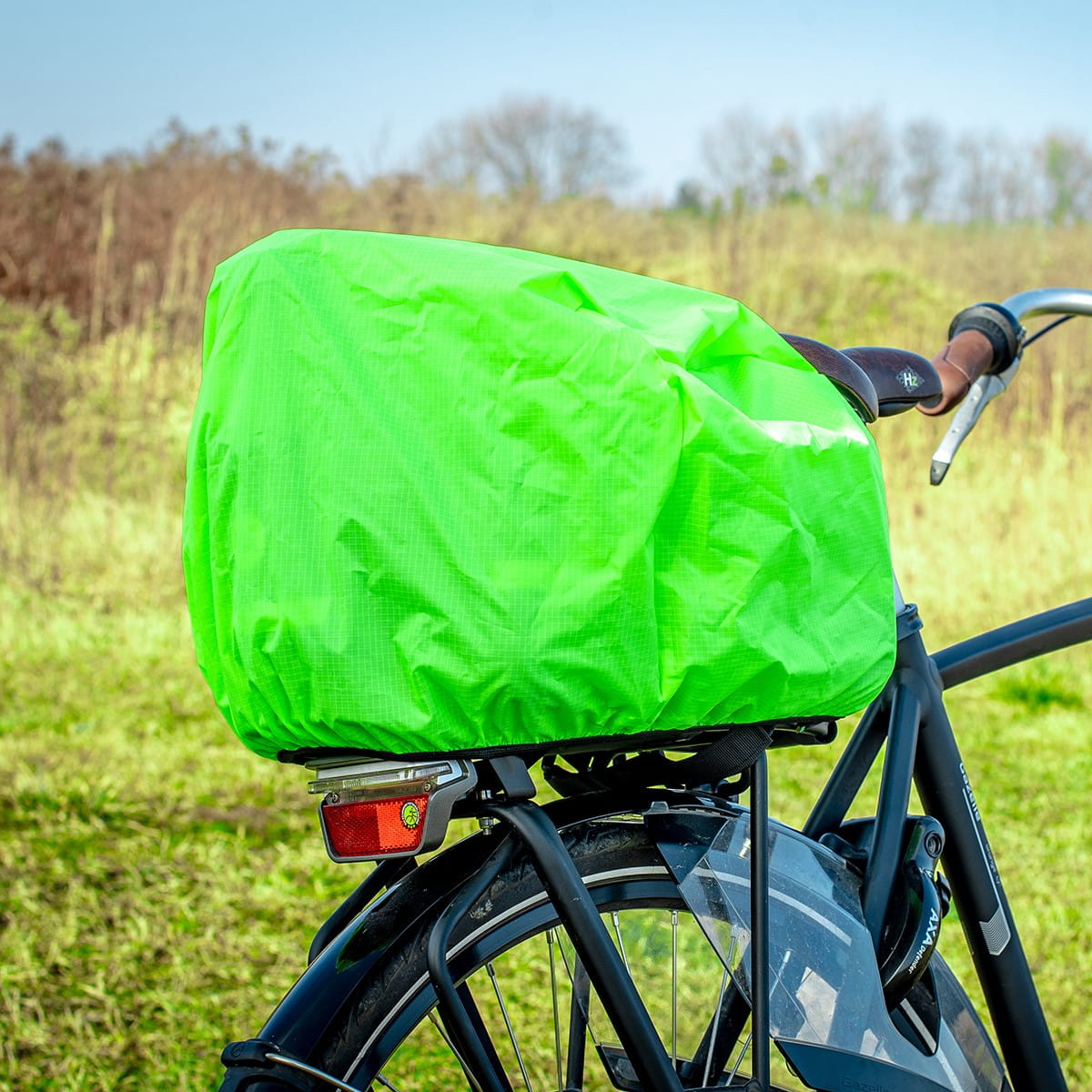 Zielona osłona przeciwdeszczowa na siodełku rowerowym. Tło to zielone pole.