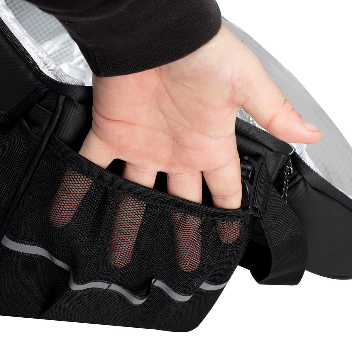 Ręka sięgająca do siatkowej kieszeni. Czarna torba, widoczne paski odblaskowe.