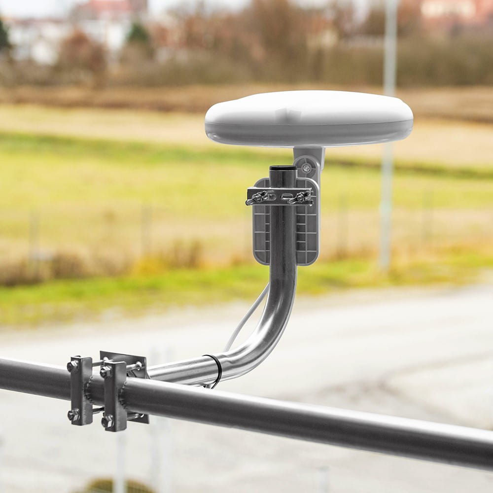 Antena satelitarna zamontowana na metalowej balustradzie. Tło to rozmyty krajobraz.