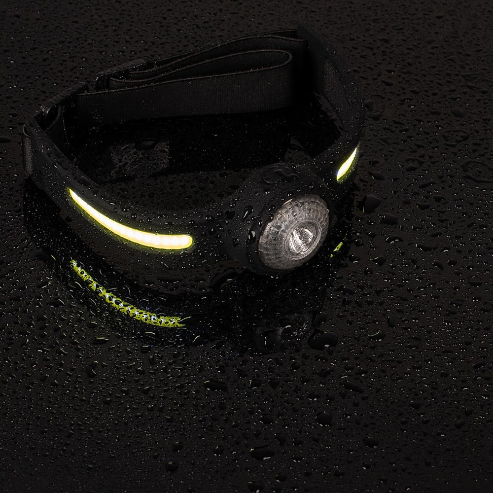 Czarna lampa czołowa z żółtymi światłami na mokrej, czarnej powierzchni. Widoczne krople wody.