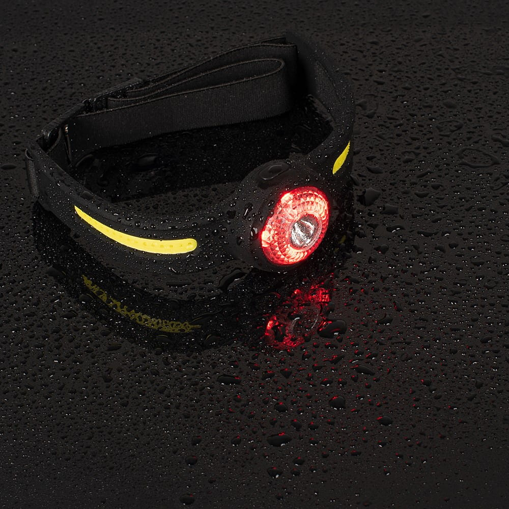 Czarna lampa czołowa na czarnej mokrej powierzchni. Lampa ma czerwone światło i czarny pasek.