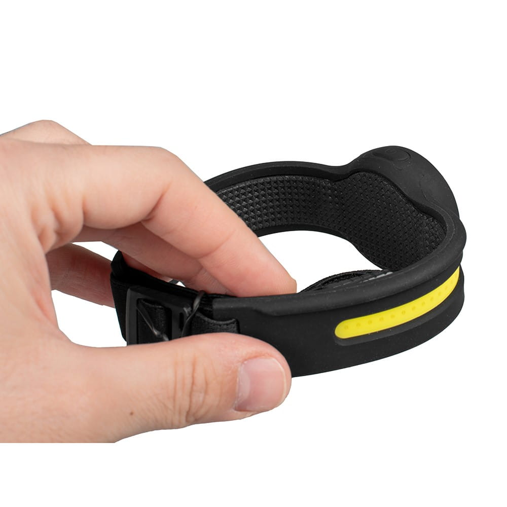 Dłoń trzymająca czarno-żółtą lampę czołową. Lampa czołowa na białym tle.