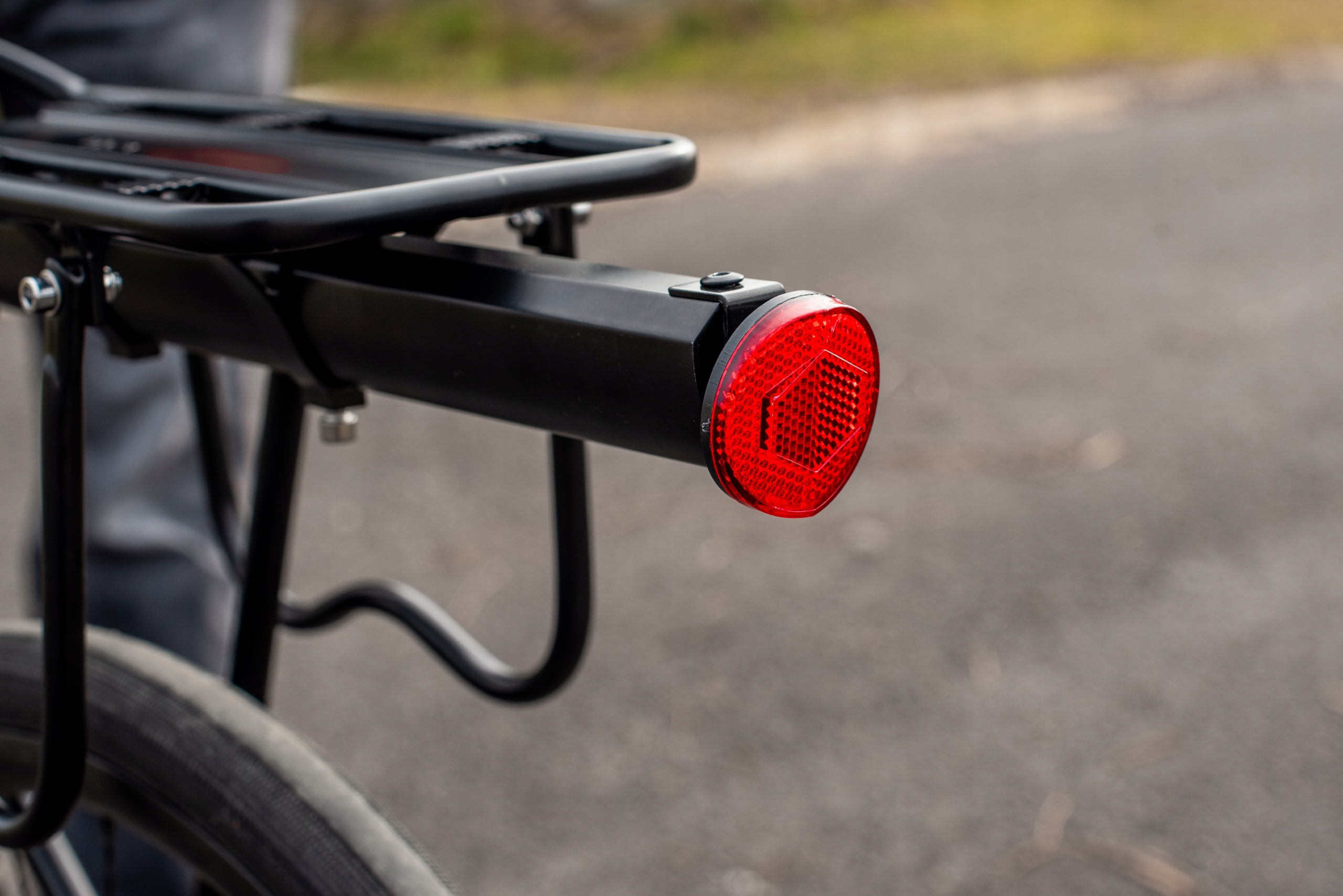 Zbliżenie bagażnika rowerowego z czerwonym tylnym światłem. Bagażnik jest czarny, a tło rozmyte.