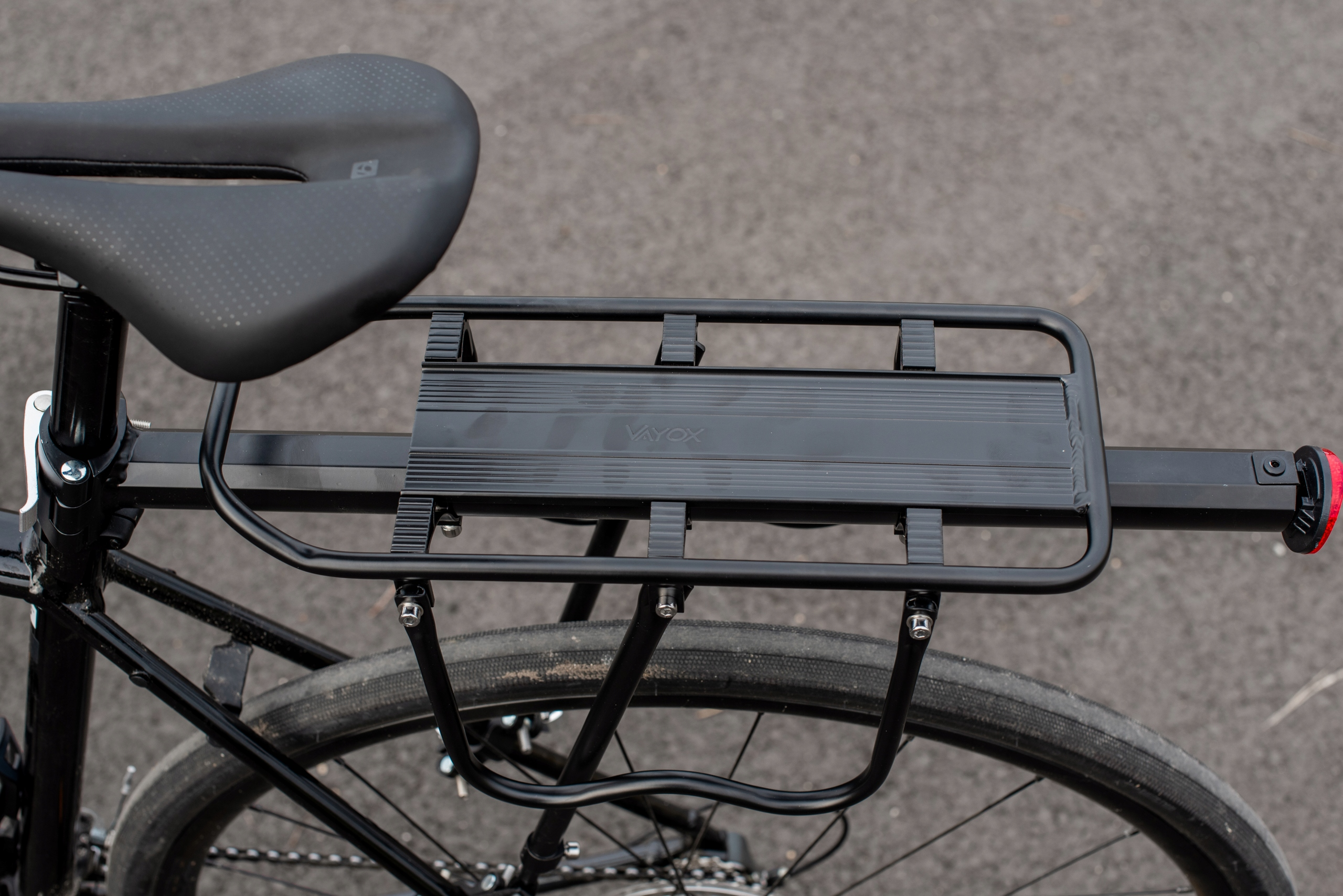 Bagażnik rowerowy na rowerze. Bagażnik jest czarny i ma czarne siodełko. Tło jest rozmyte.