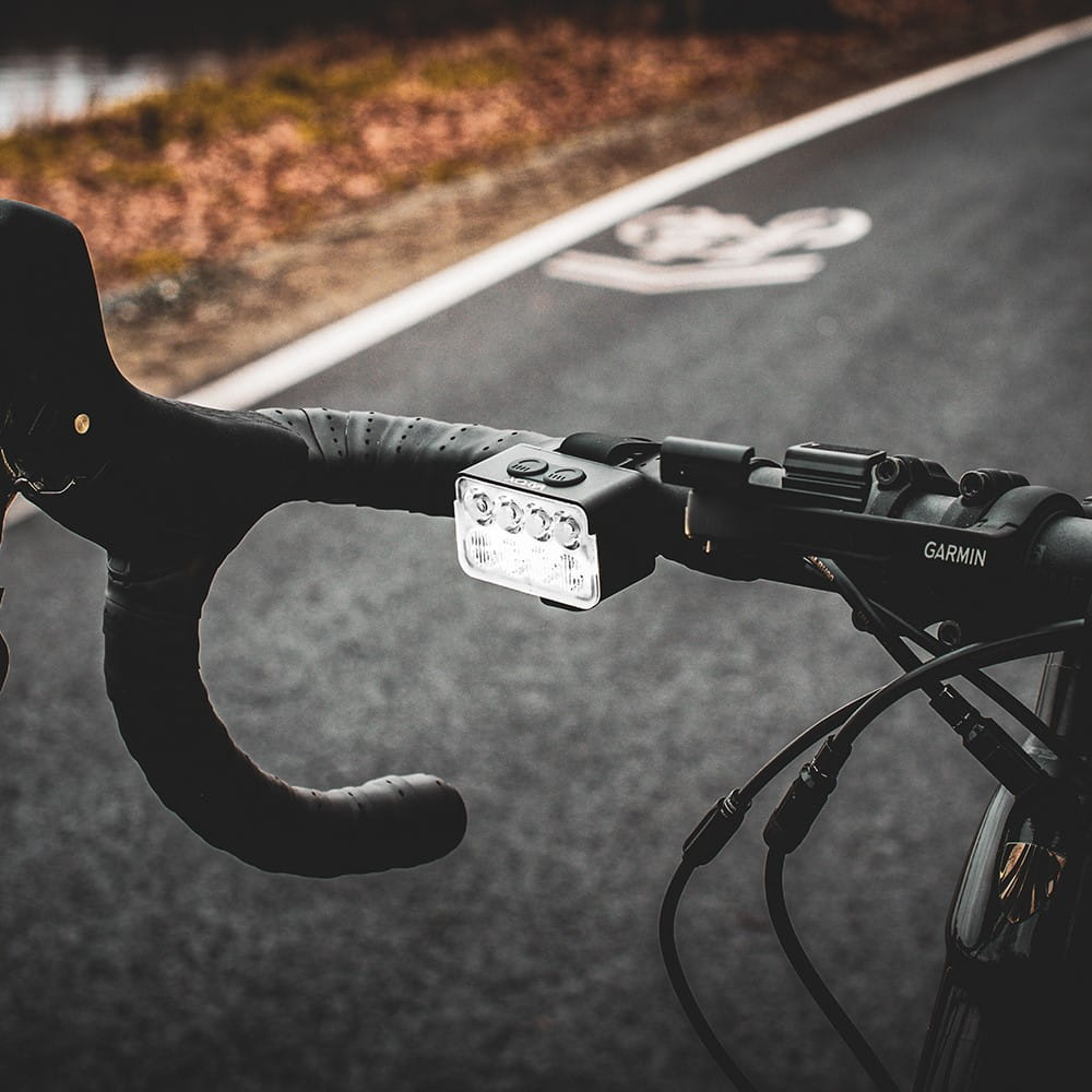Kierownica roweru z przednim światłem. Światła są włączone. Droga w tle.