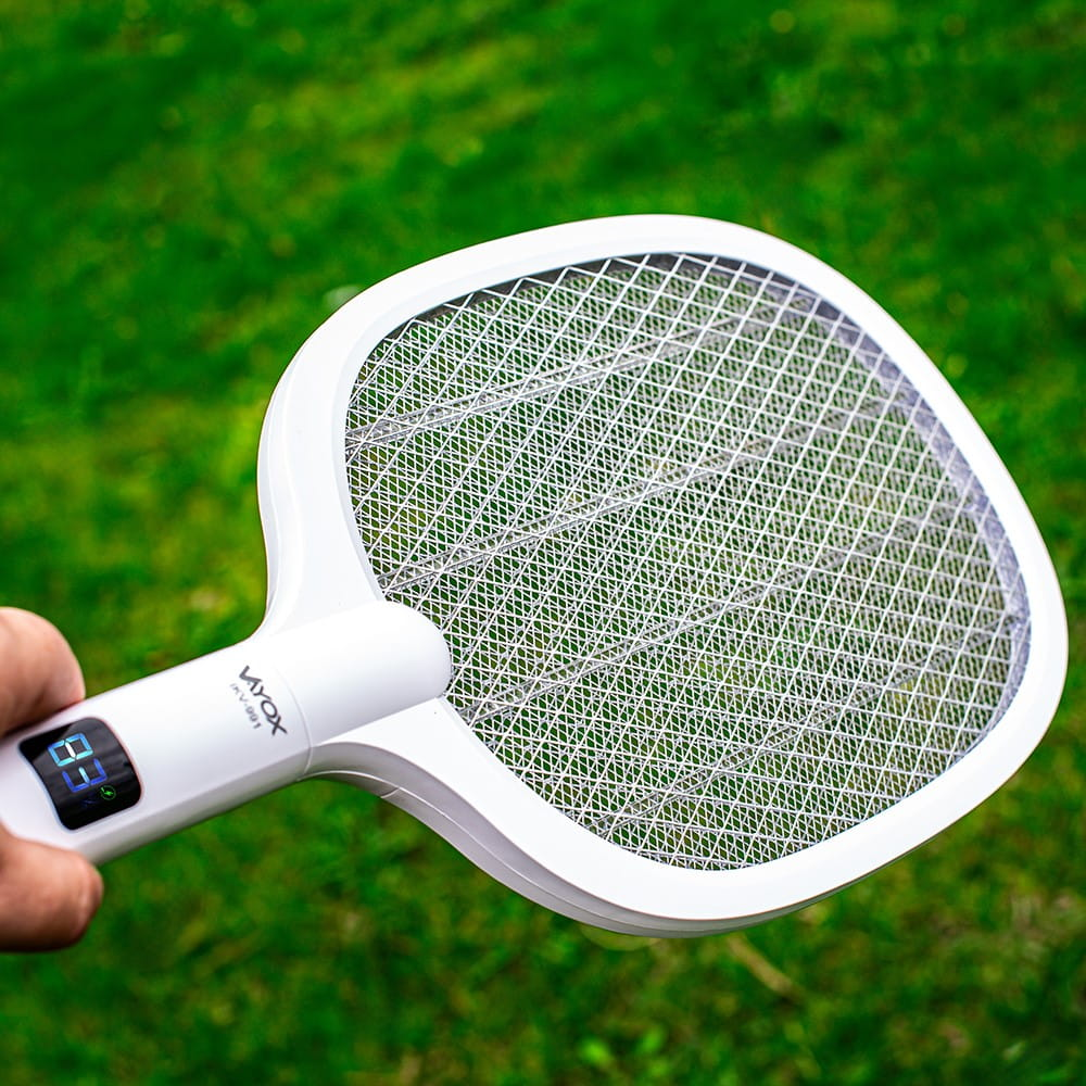 Ręka trzyma białą packę na muchy Vayox nad trawą. Wyświetlacz pokazuje 83.