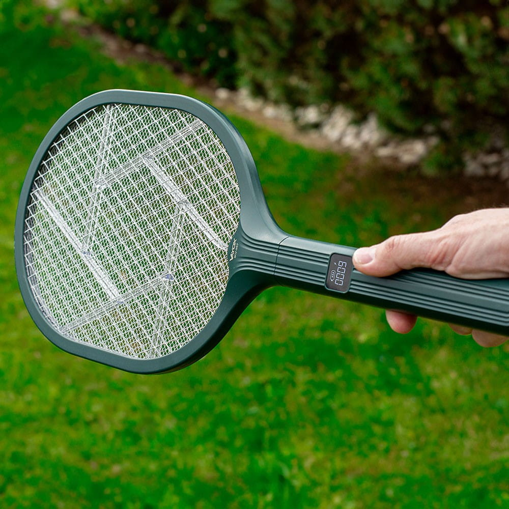 Ręka trzymająca zieloną elektryczną packę na komary, pokazująca wyświetlacz cyfrowy i siatkę.