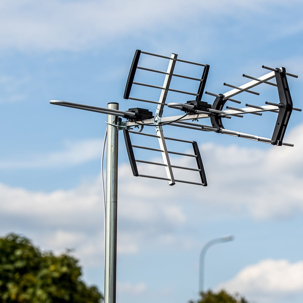 Antena TV stoi na tle błękitnego nieba z chmurami. Antena jest srebrna i czarna.