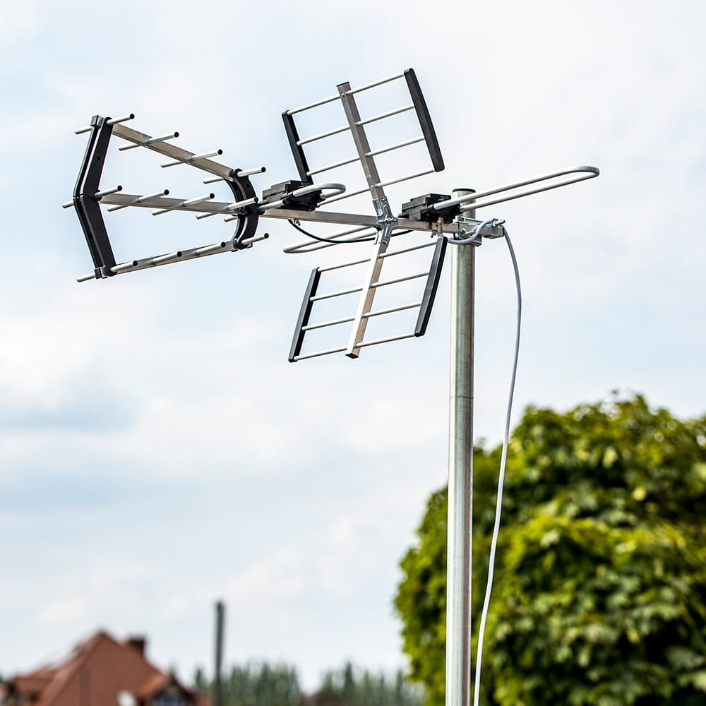 Antena zewnętrzna na maszcie. Tło czystego nieba. Widoczne drzewa i dom.