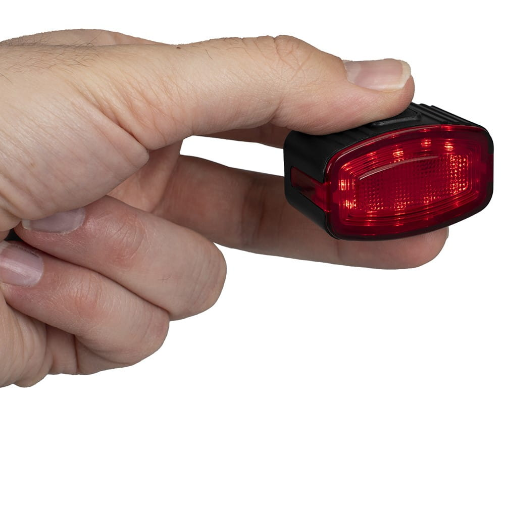 Ręka trzyma małą, czerwoną lampkę rowerową. Światło jest włączone i świeci.
