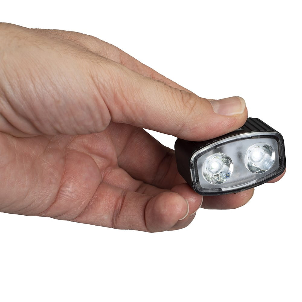 Ręka trzyma małą lampkę rowerową. Widoczne są dwa białe światła.