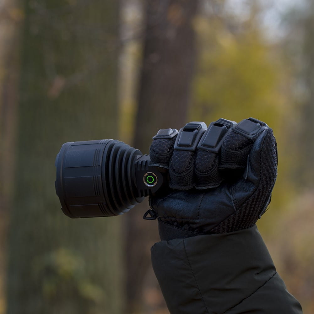Czarna latarka trzymana w rękawicy, rozmyte zielone tło.