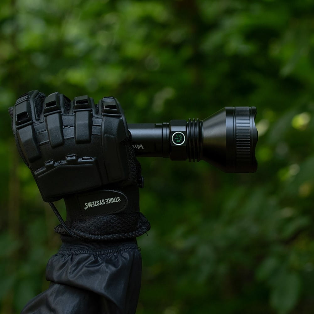 Czarna latarka trzymana w rękawicy, rozmyte zielone tło.