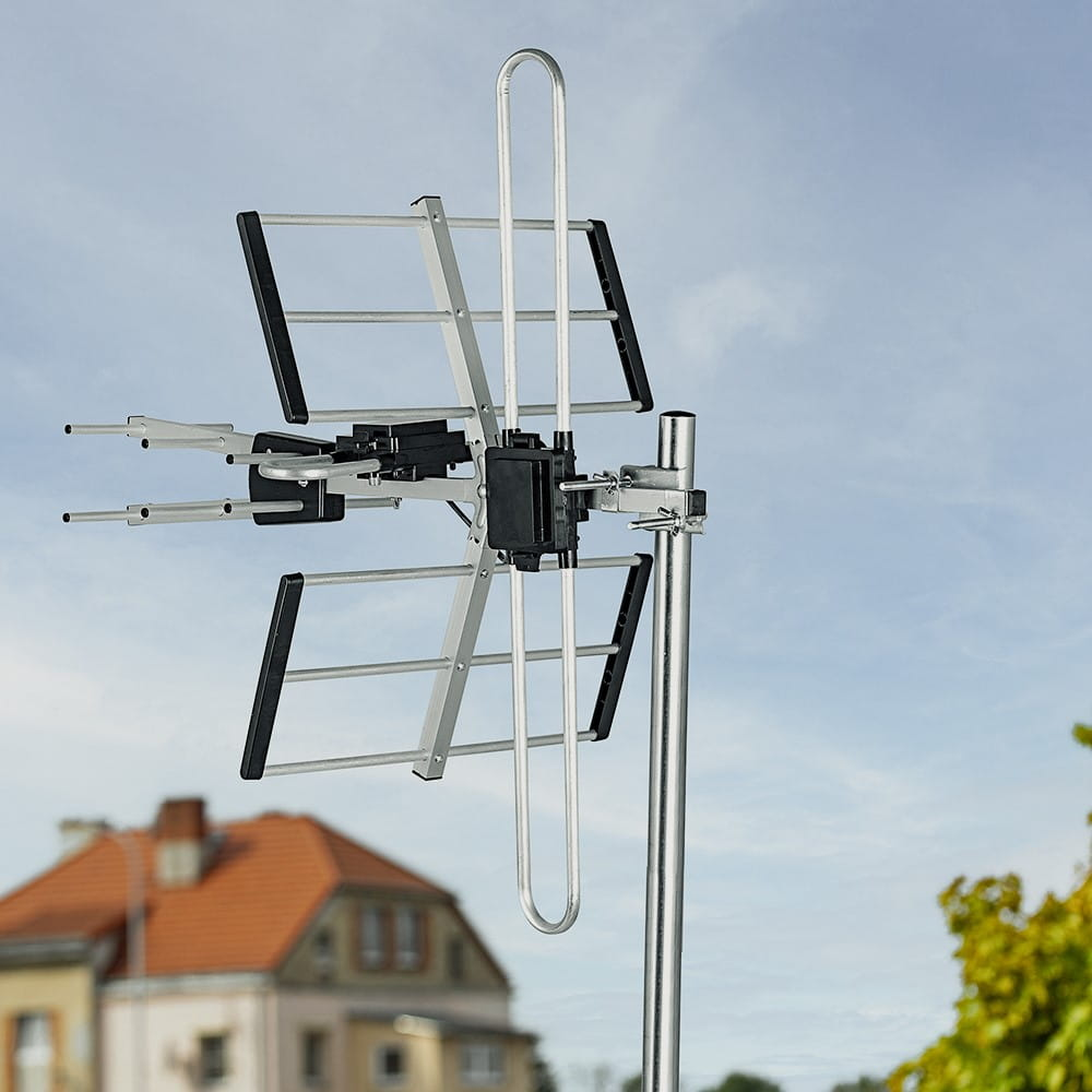 Antena TV zamontowana na słupie na zewnątrz budynku. Na tle widoczne jest niebo.