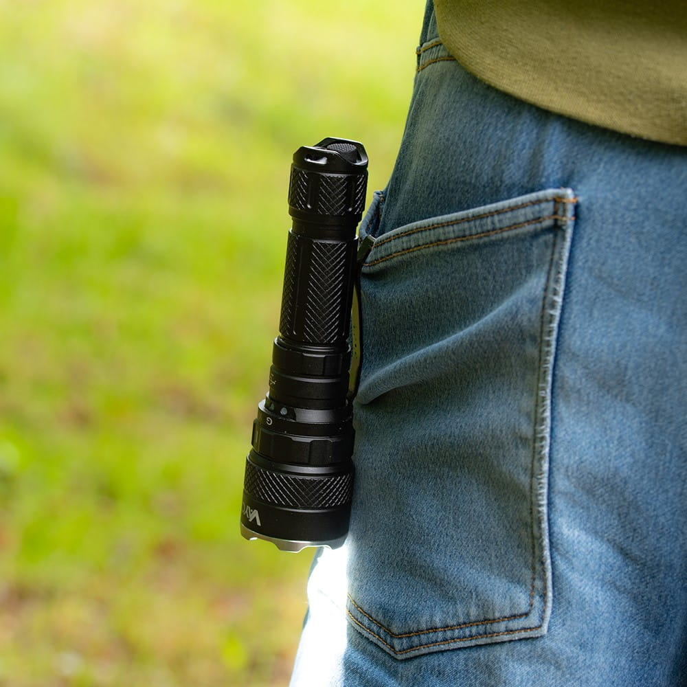 Czarna latarka przypięta do tylnej kieszeni niebieskich dżinsów, zielone tło.