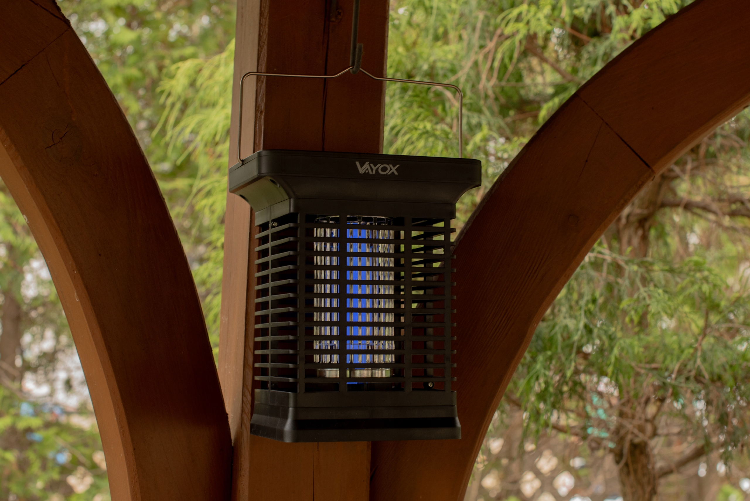 Czarny zabójca owadów zawieszony na drewnianej konstrukcji; emituje niebieskie światło.