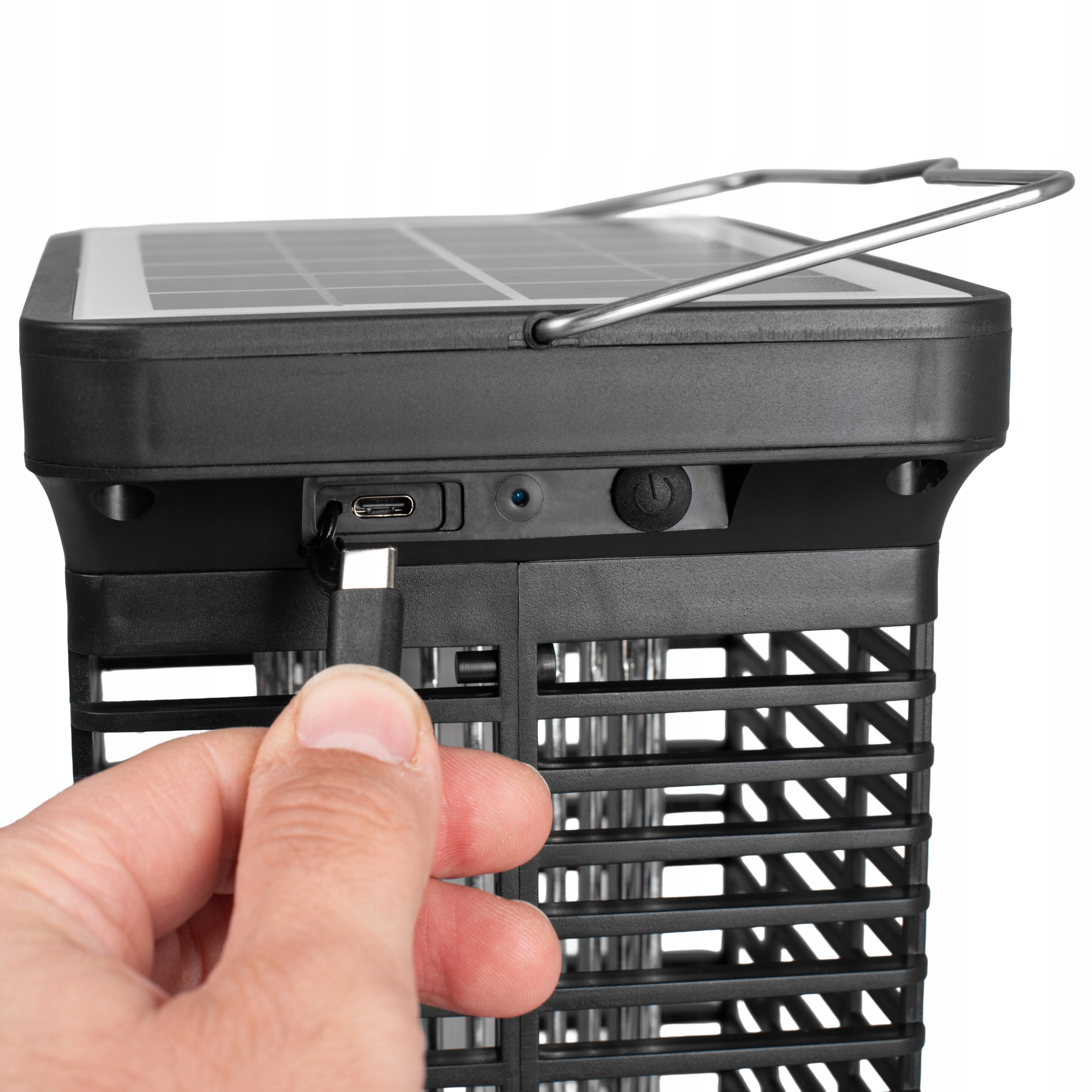 Dłoń podłączająca kabel USB-C do czarnej solarnej lampy na komary, białe tło.