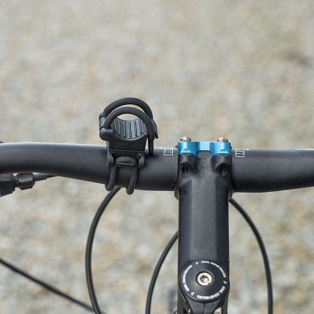 Czarny uchwyt na światło rowerowe przymocowany do czarnej kierownicy z niebieskimi akcentami.