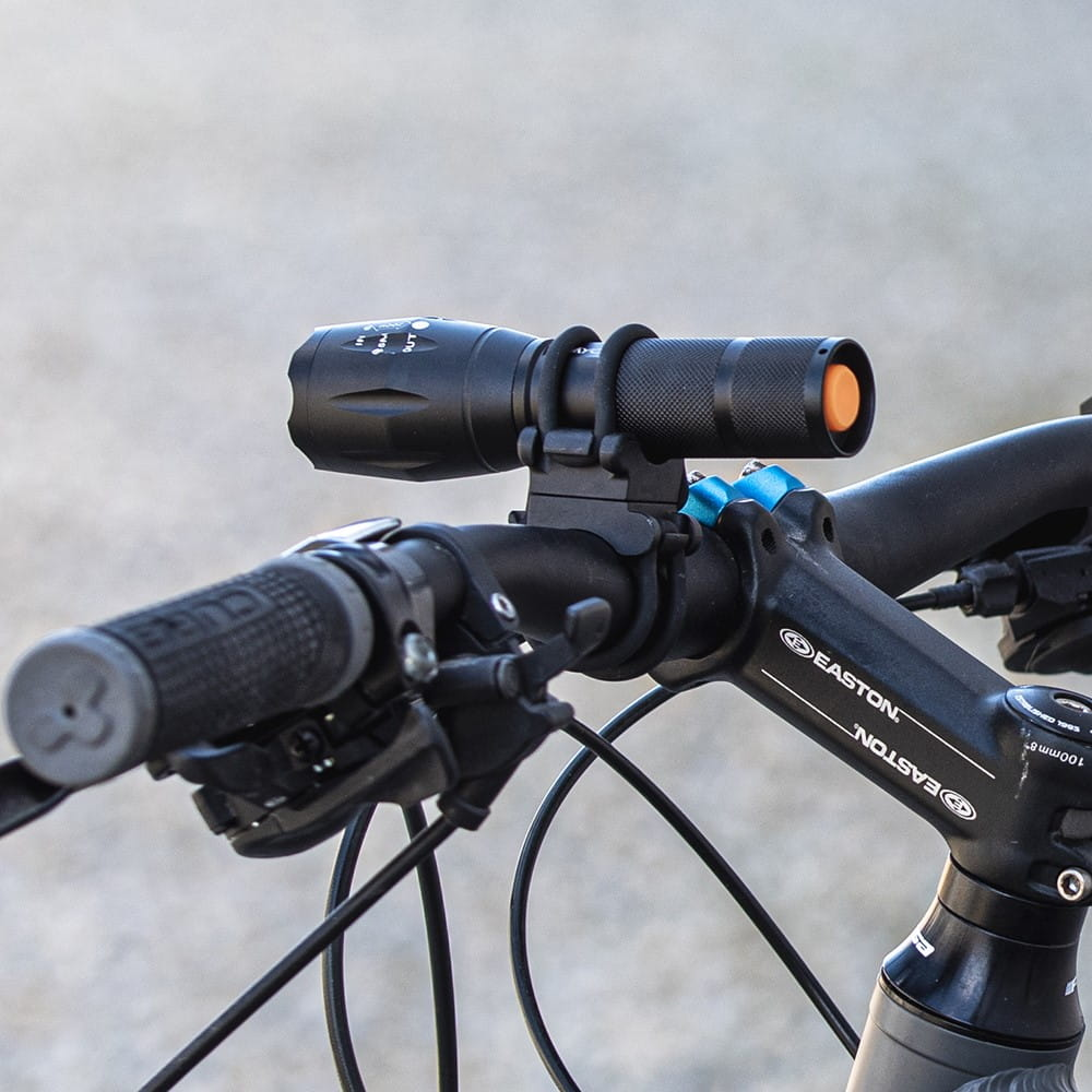 Czarna latarka zamontowana na kierownicy roweru, z niebieskim mocowaniem. Na zewnątrz.