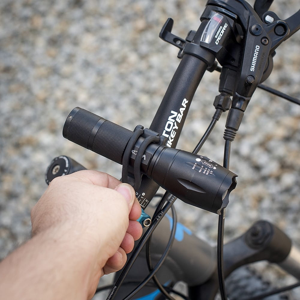 Ręka osoby trzymającej czarną lampkę rowerową przymocowaną do kierownicy.