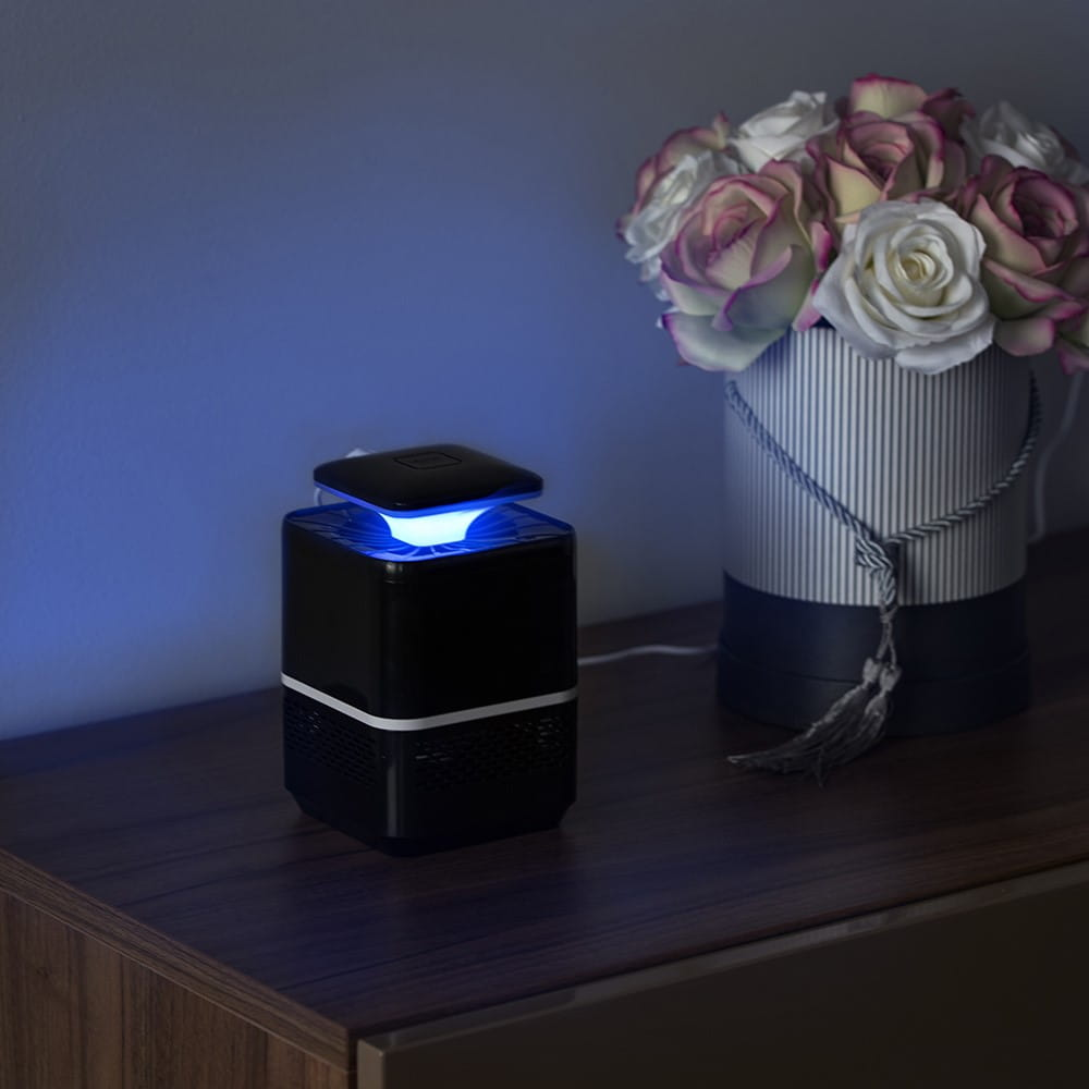 Czarna lampa do zabijania owadów z niebieskim światłem. Białe tło. Róże na stole.